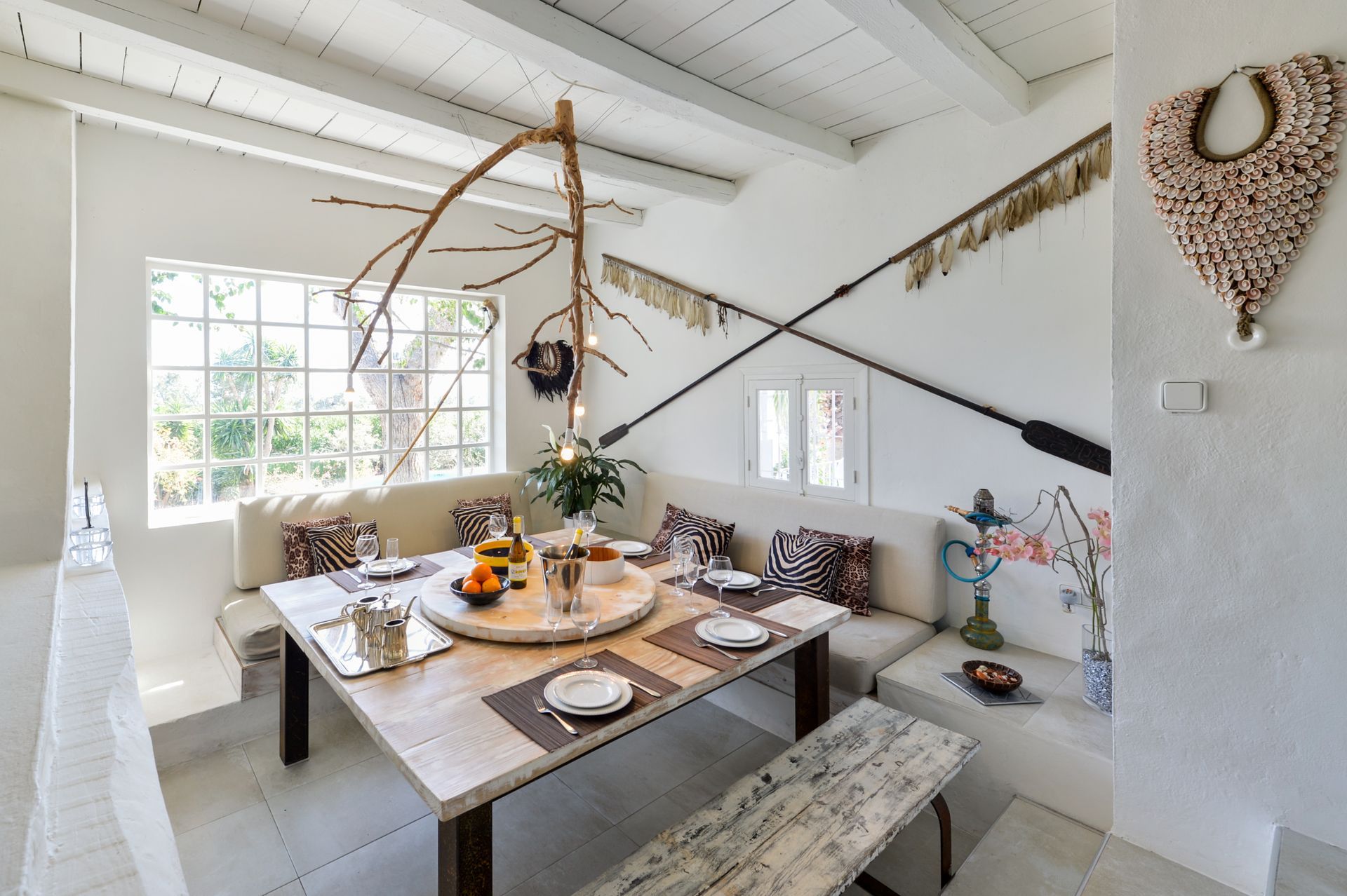 Comedor con paredes y muebles blancos. Mesa preparada para comer; elementos decorativos en las paredes.
