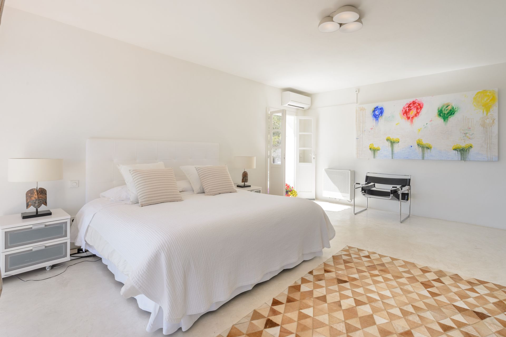 Dormitorio blanco brillante con una cama, obras de arte y una alfombra geométrica.