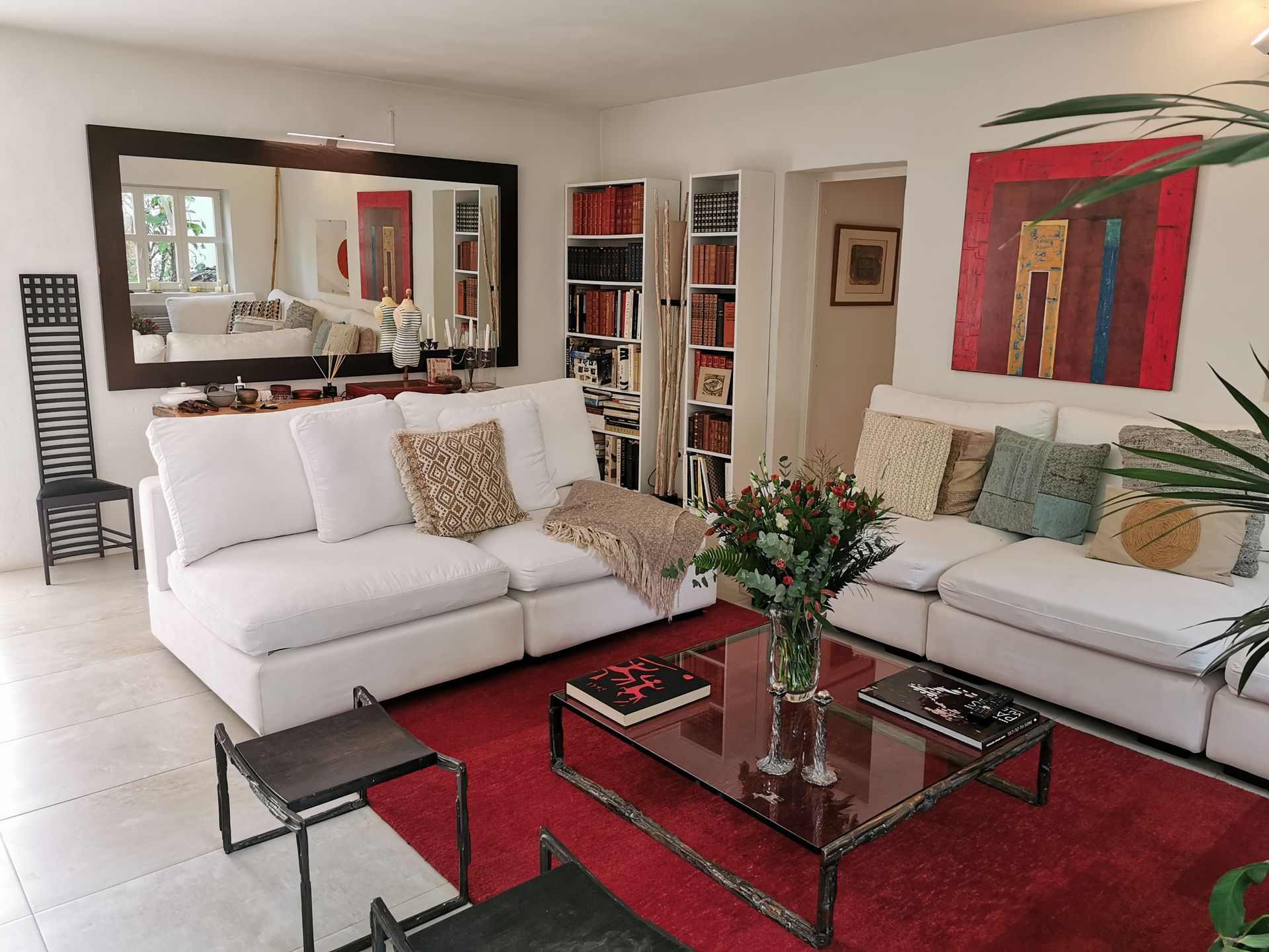 Sala de estar con sofás blancos, alfombra roja, libros y arte.