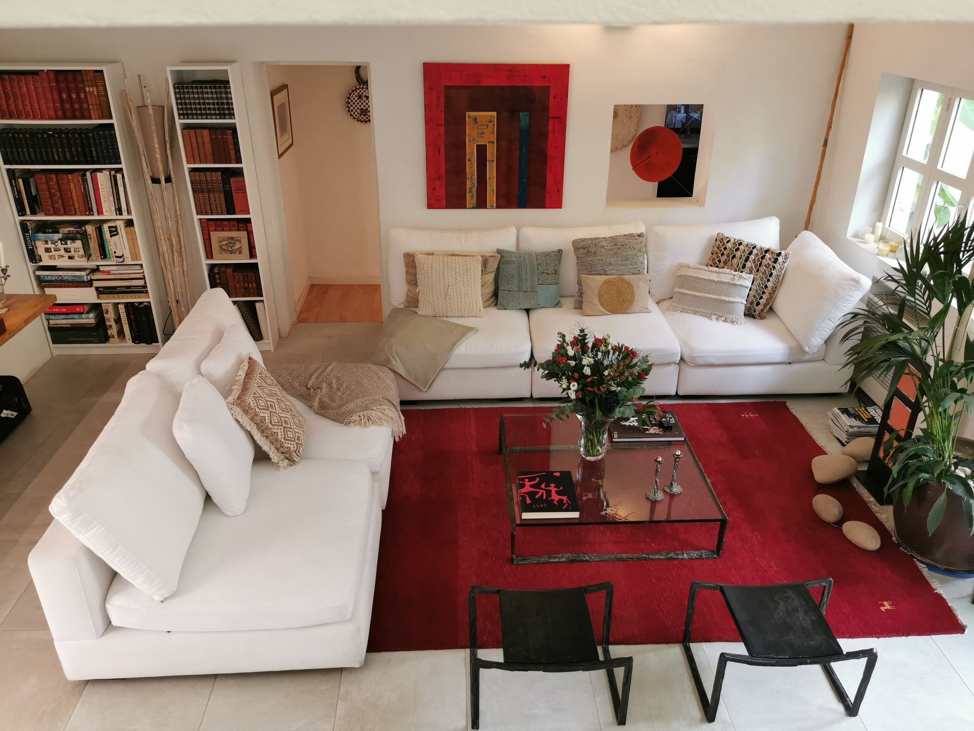 Sala de estar con sofás blancos, alfombra roja, arte y sillas negras.