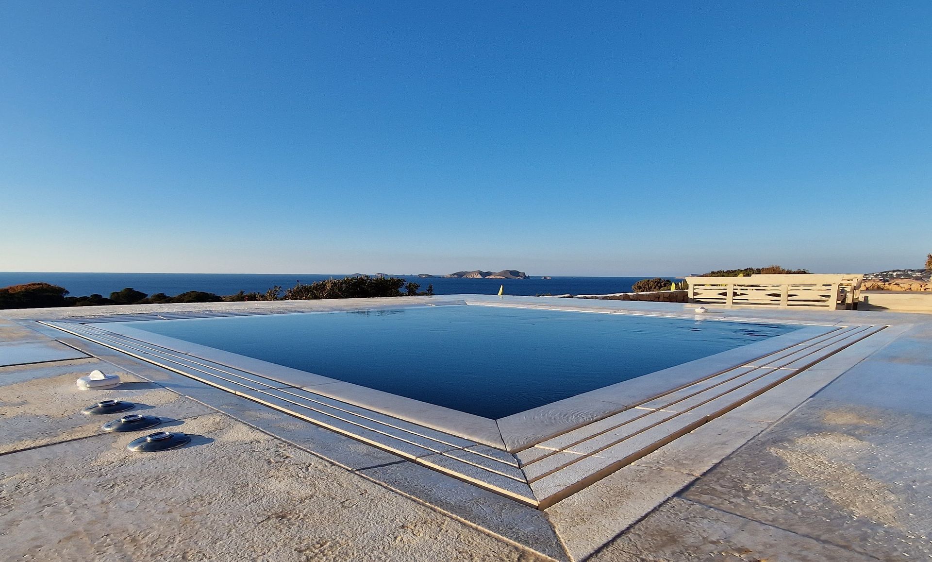 Piscina de agua azul con vistas al mar y cielo despejado. Edificio a la derecha.