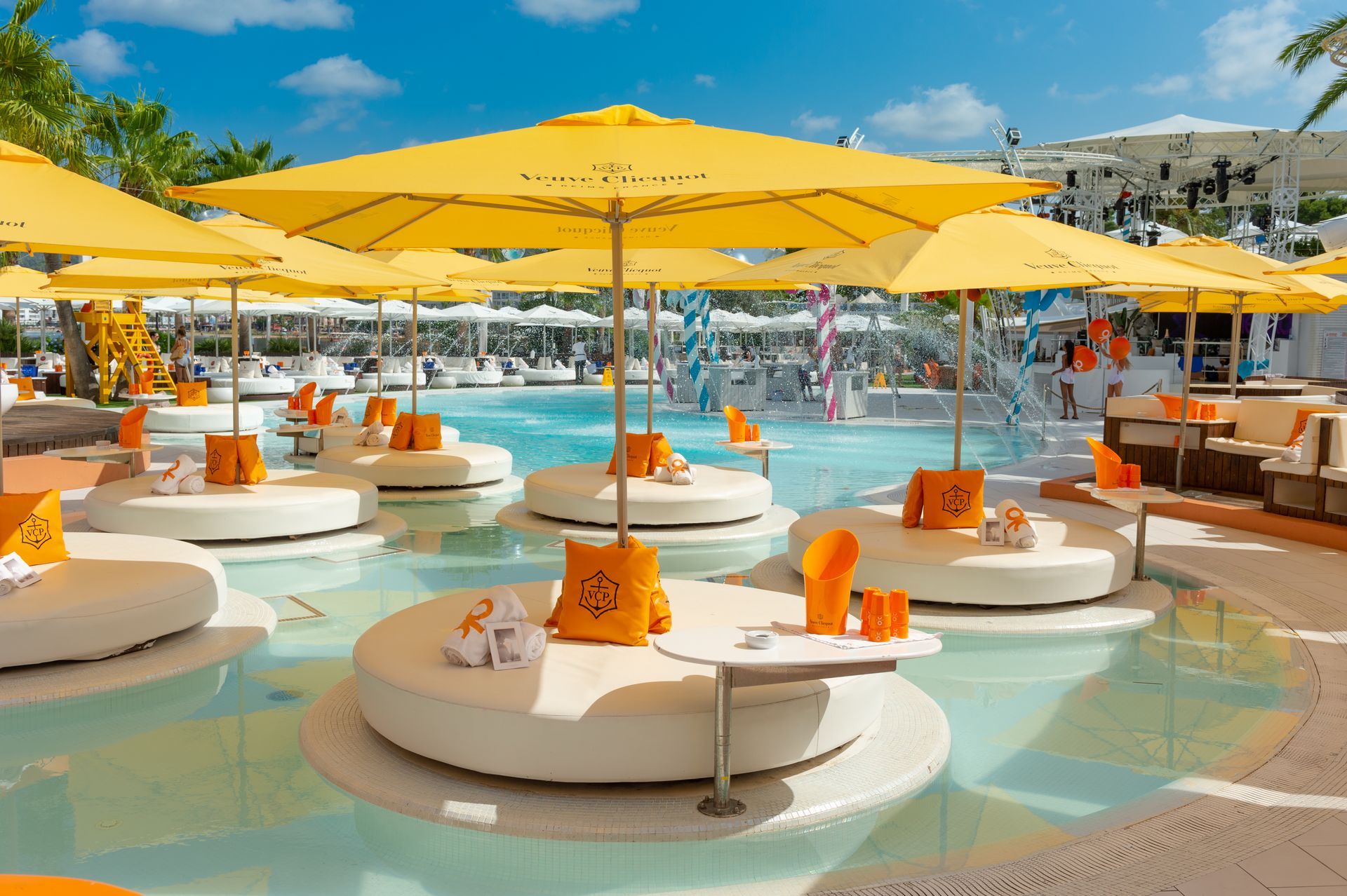 Sombrillas amarillas dan sombra a las tumbonas blancas en una piscina; un complejo turístico soleado.