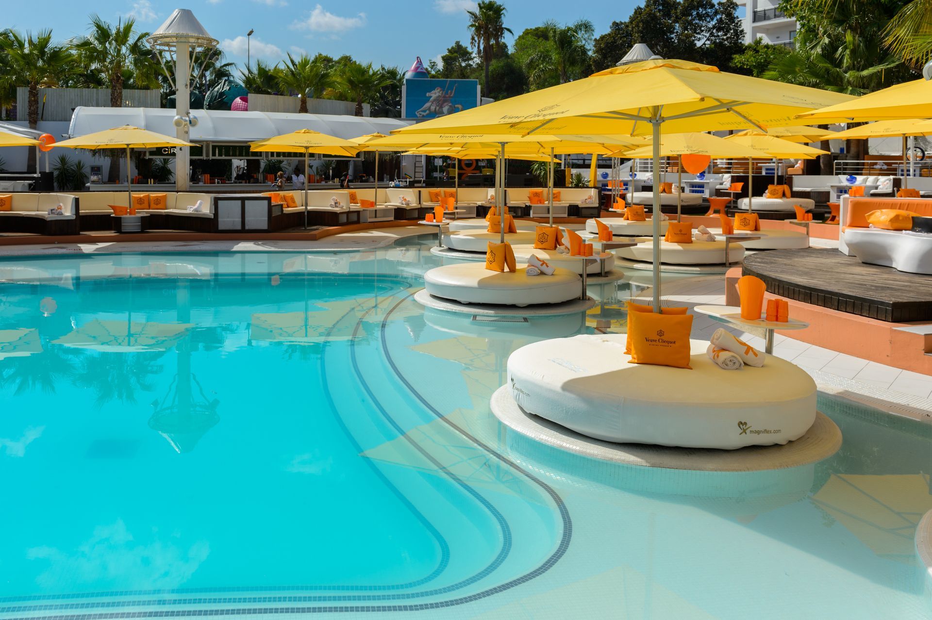 Piscina con sombrillas amarillas y zonas de descanso blancas.
