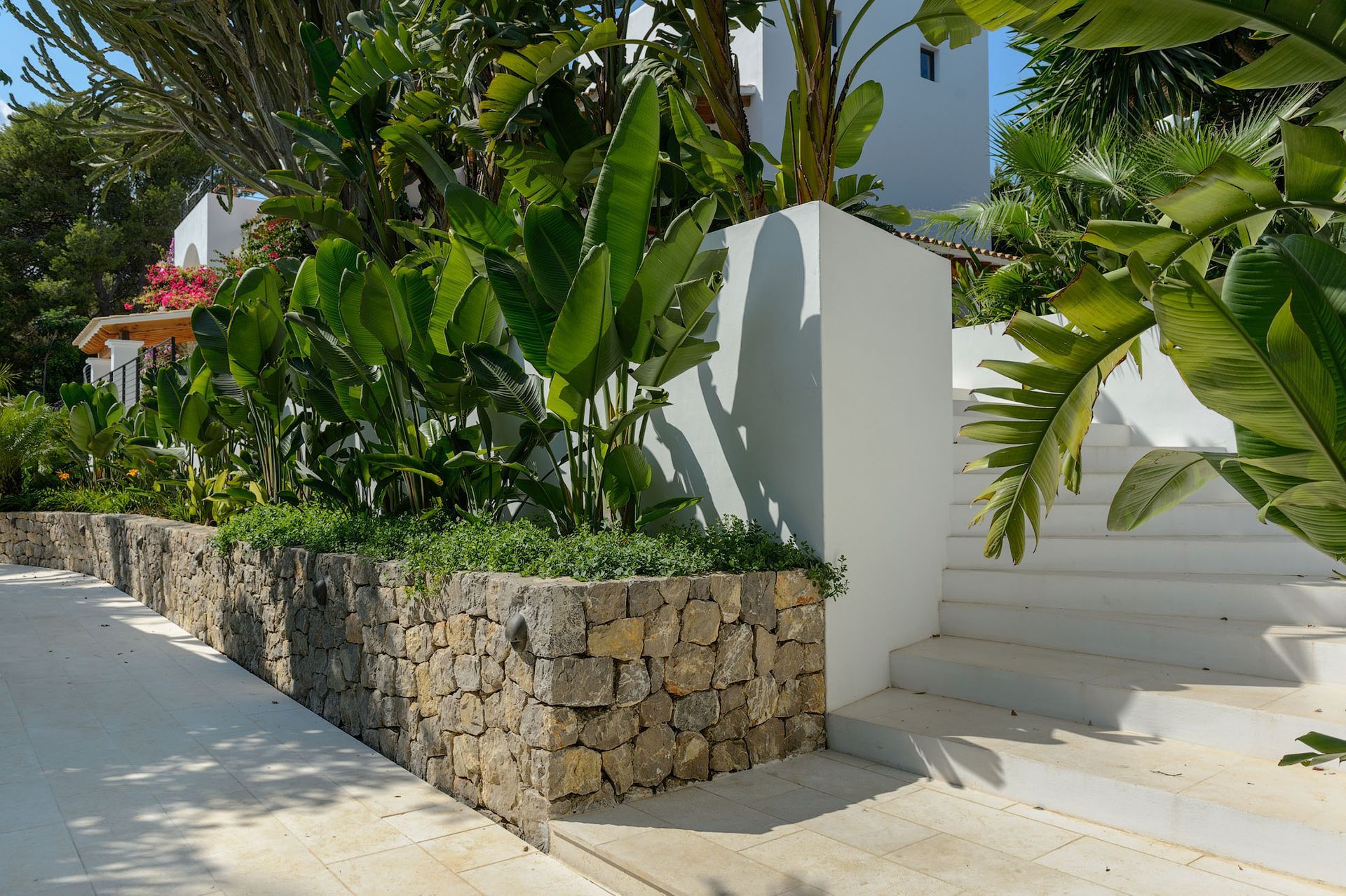 Muro de contención de piedra con exuberante vegetación y escaleras blancas.