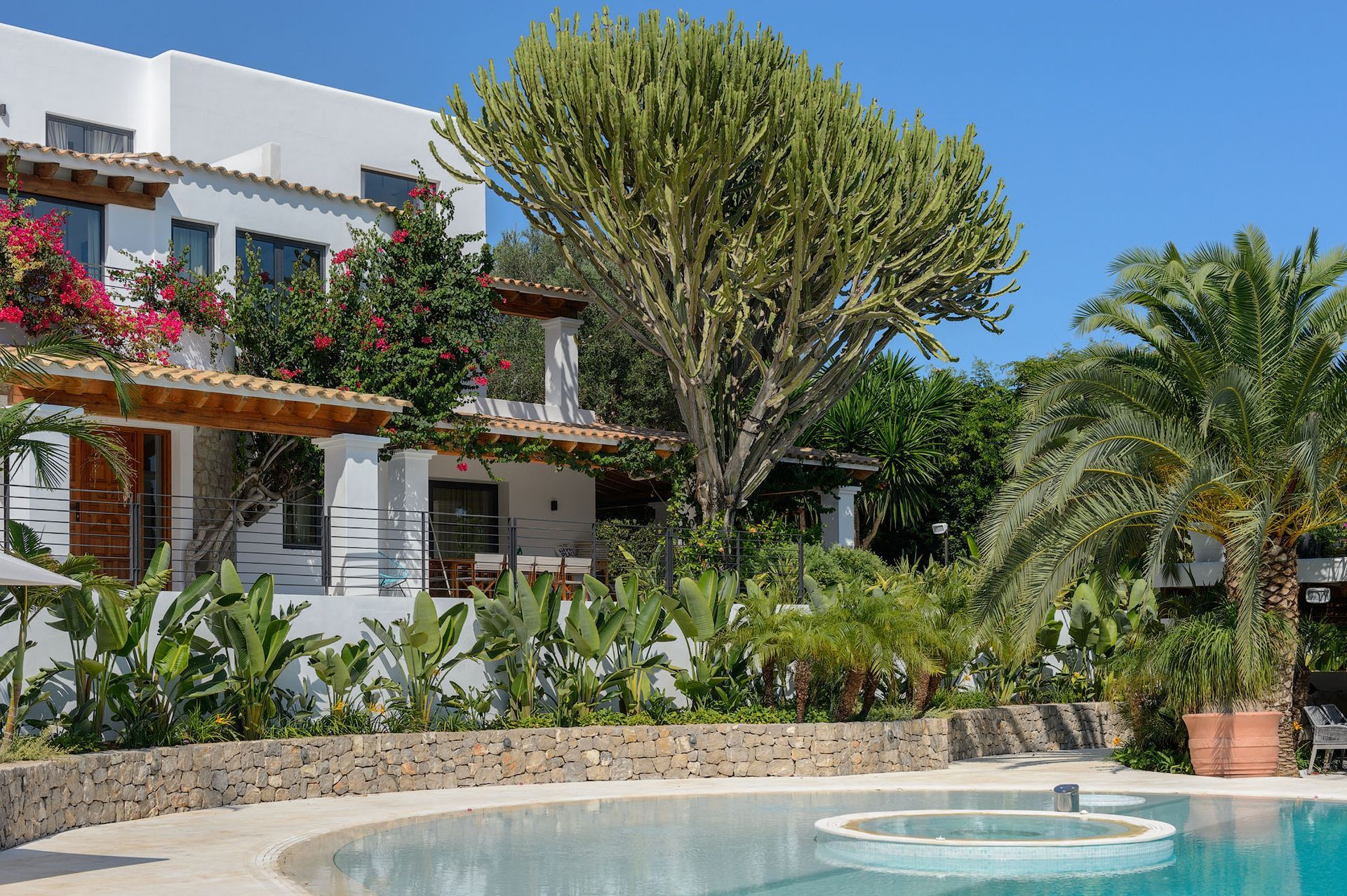 Edificio blanco con piscina y exuberante vegetación bajo un cielo azul claro.