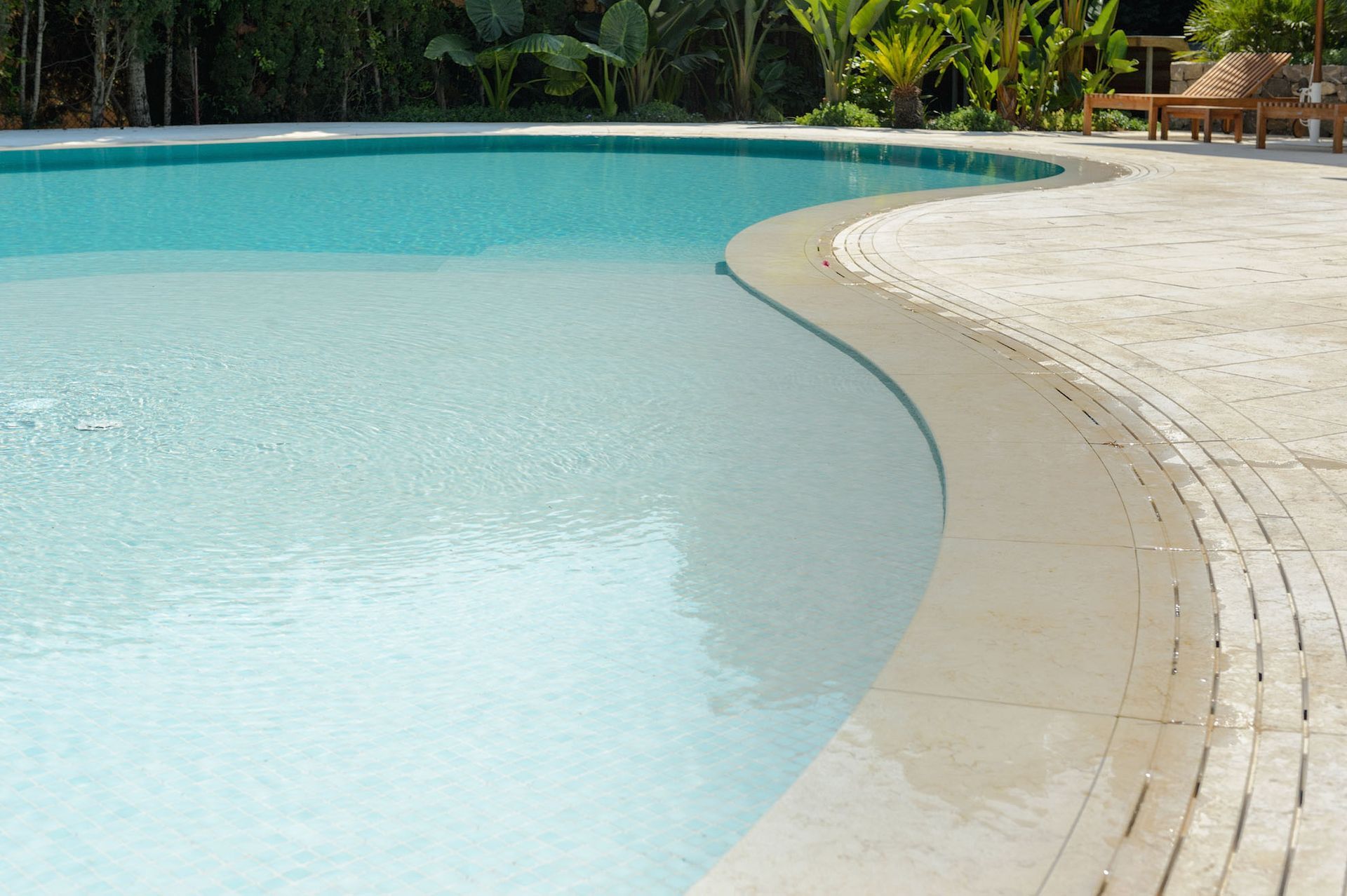 Piscina de agua clara, borde curvo y pavimento de color claro.