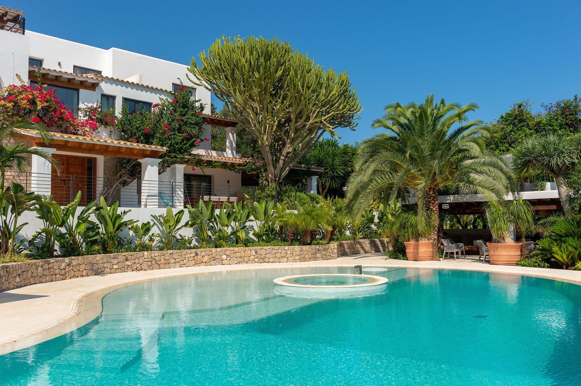 Piscina frente a un edificio blanco con un exuberante paisaje. Cielo azul despejado.