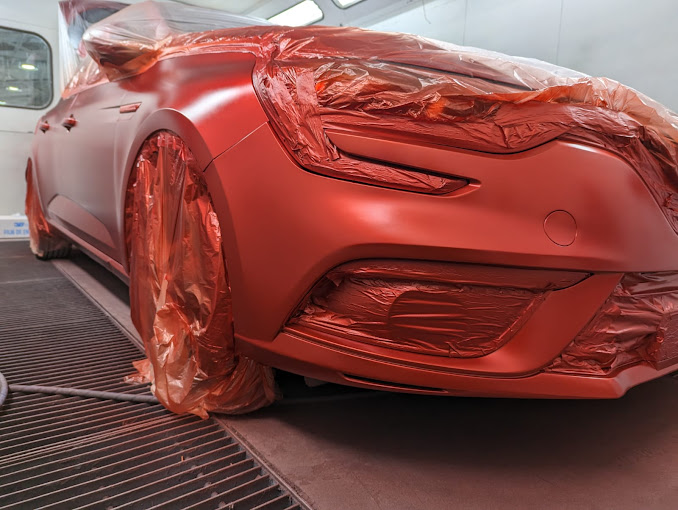 Un coche rojo está cubierto con una envoltura de plástico en una cabina de pintura.