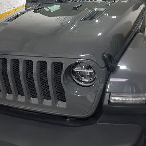 Un jeep gris está estacionado en un garaje con el capó levantado.