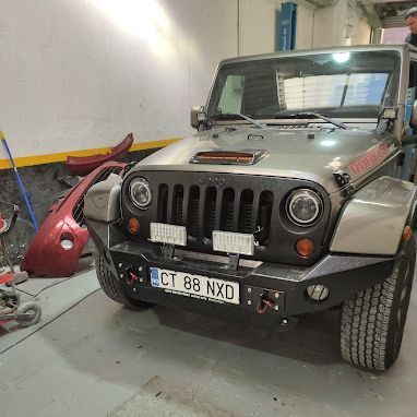 Un jeep está estacionado en un garaje al lado de un parachoques rojo.