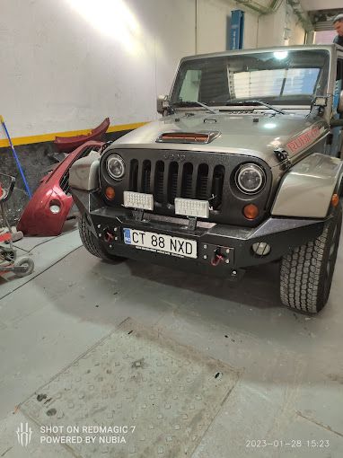 Un jeep está estacionado en un garaje al lado de un parachoques rojo.
