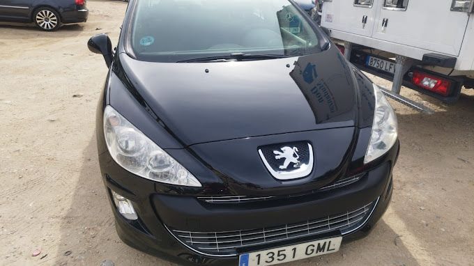 Un coche Peugeot negro está aparcado en un aparcamiento.