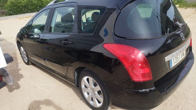 Un coche negro con una luz trasera roja está estacionado al costado de la carretera.