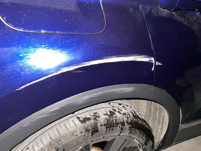 Un coche azul con un guardabarros y un neumático dañados.