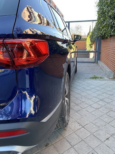 Un coche azul está aparcado en una entrada junto a una pared de ladrillos.