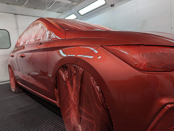 Se está pintando un coche rojo en una cabina de pintura.