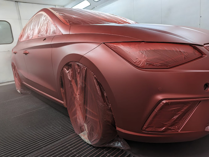 Se está pintando un coche rojo en una cabina de pintura.