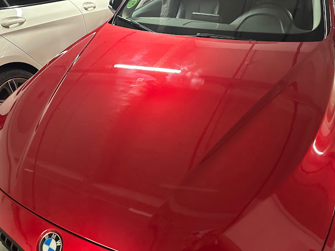Un BMW rojo está aparcado en un garaje al lado de un coche blanco.