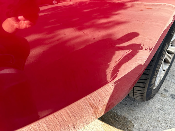 Un coche rojo está estacionado al costado de la carretera.