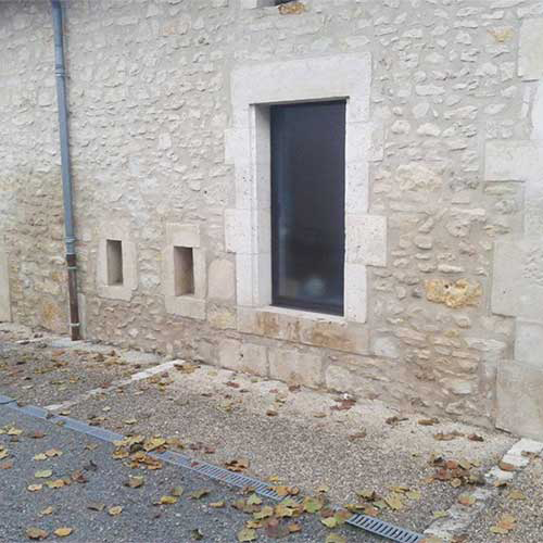 Mur blanc avec fenêtre montrant des traces d'humidité avec la partie basse plus sombre que la partie haute