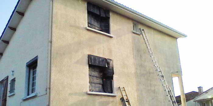 Traitement de l'humidité en façade d'une maison en cours montrant une partie saine et une partie sombre