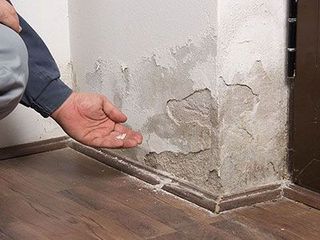 Personne agenouillée tenant des bouts de mur effrité à la suite des dégâts de l'humidité