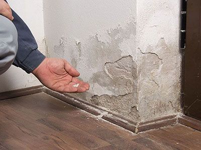 Personne agenouillée tenant des bouts de mur effrité à la suite des dégâts de l'humidité