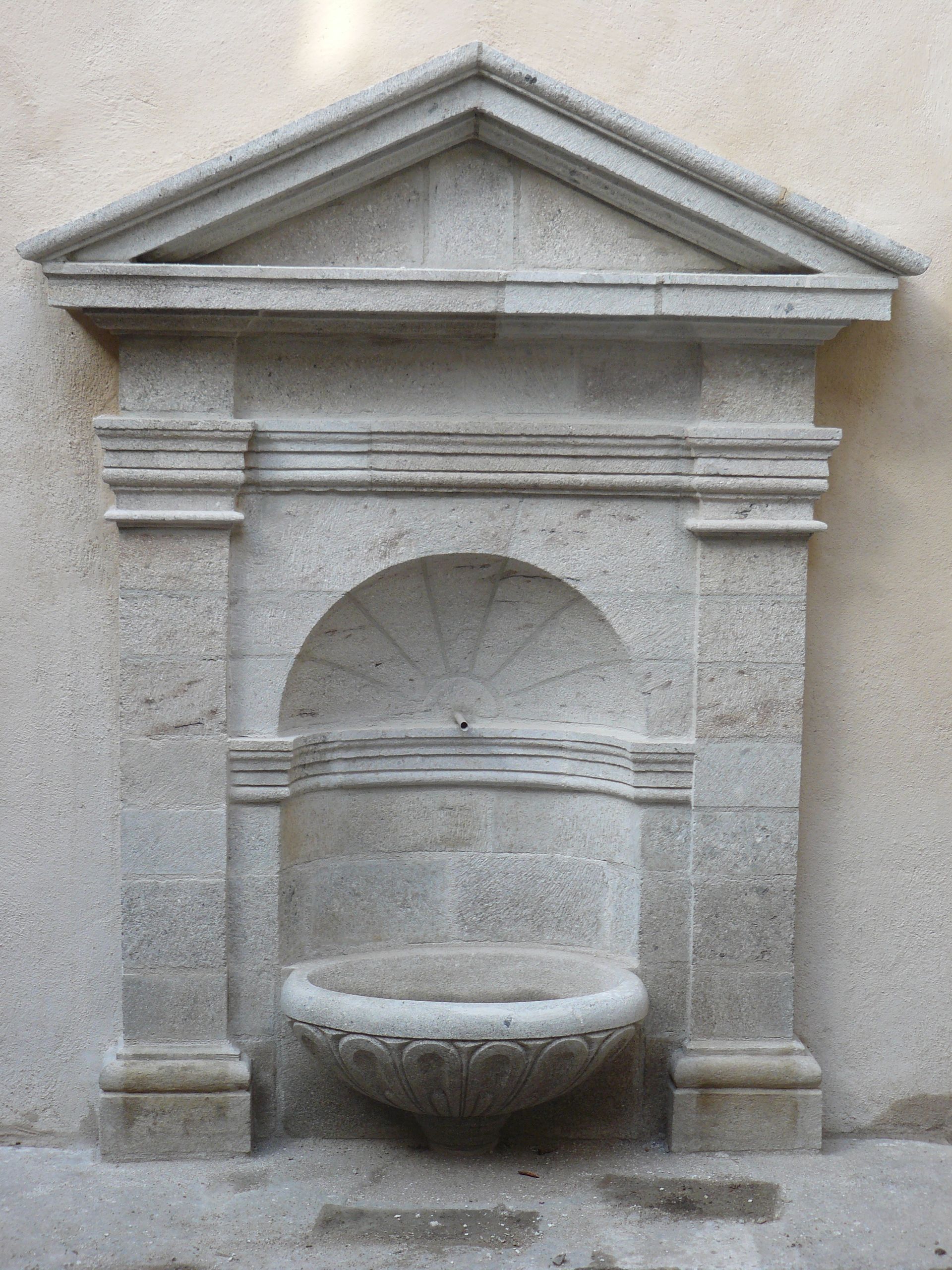 Niche de fontaine en pierre avec une alcôve cintrée et un bassin sculpté
