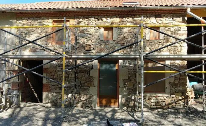 Façade en pierre d'un bâtiment avec échafaudages lors de travaux de rénovation extérieure sous une toiture en tuiles