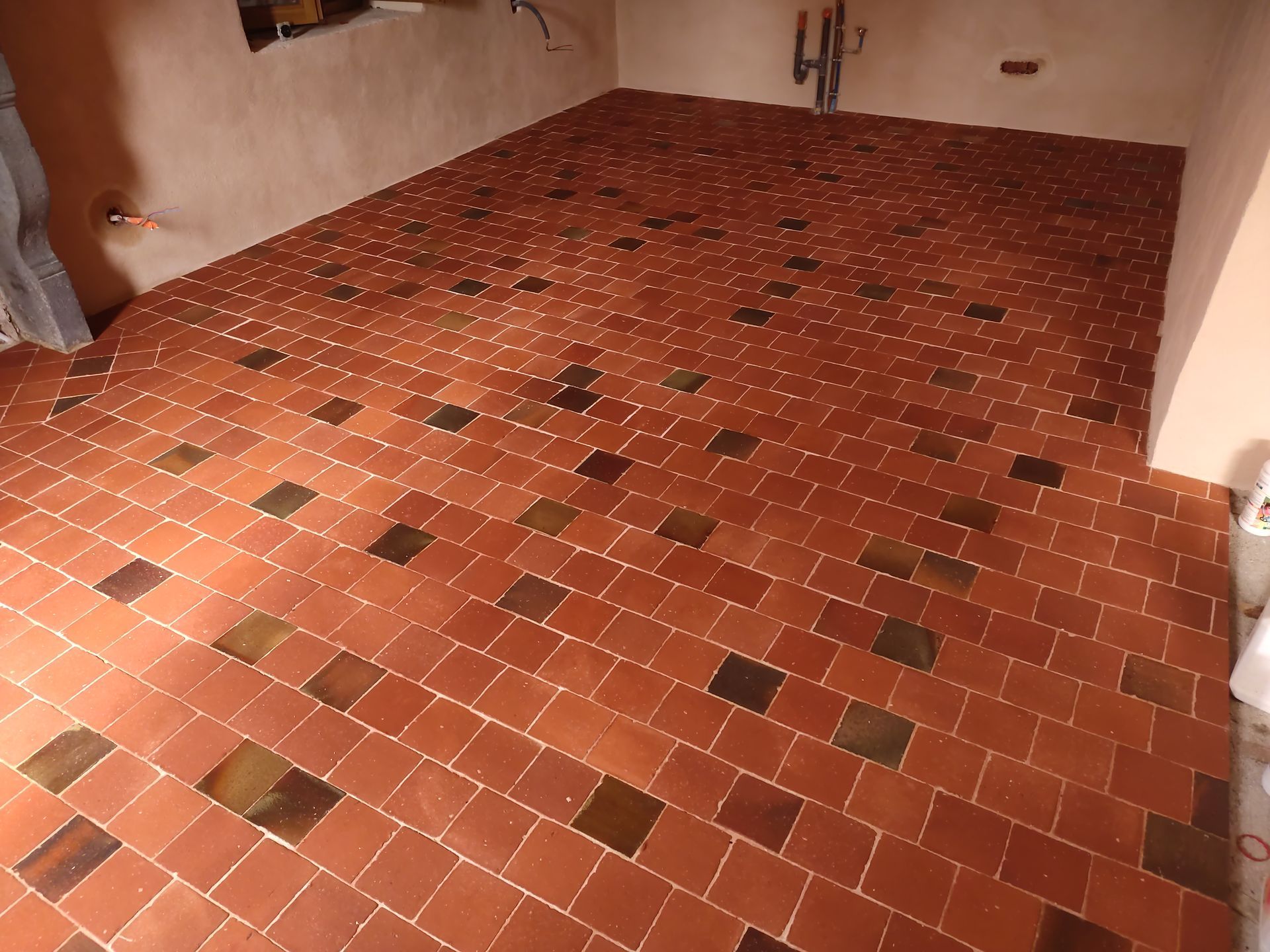 Pièce vide au sol carrelé brun rougeâtre et aux murs beiges, vue depuis la porte.