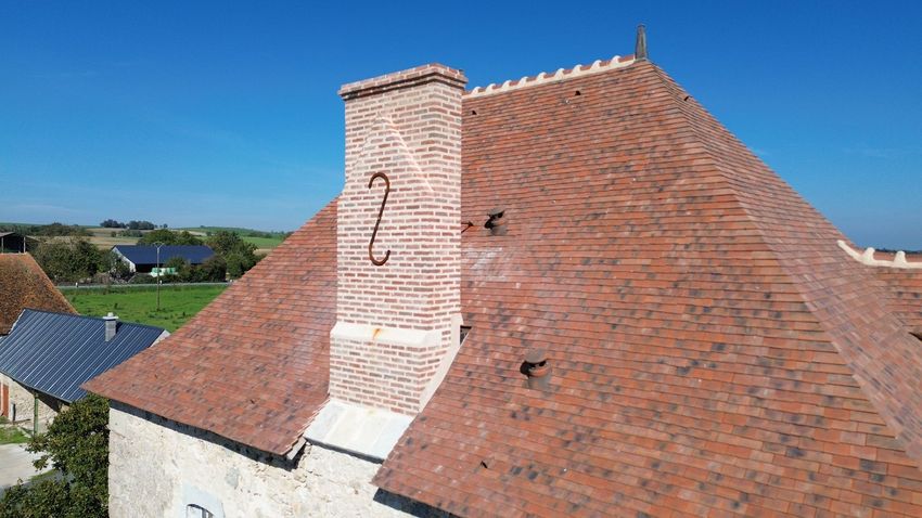Toit de tuiles rouges sur un bâtiment blanc sous un ciel bleu clair, avec la campagne en arrière-plan