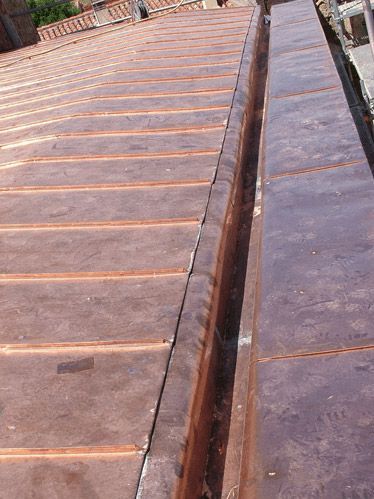 Techo de cobre con canalón tipo artesa. El techo está hecho de paneles rectangulares de color naranja óxido.