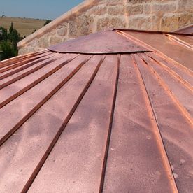 Techo de cobre con juntas verticales contra un edificio de piedra.