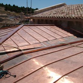 Techo de cobre con costuras visibles, construcción en ángulo y techo de tejas de arcilla cercano.