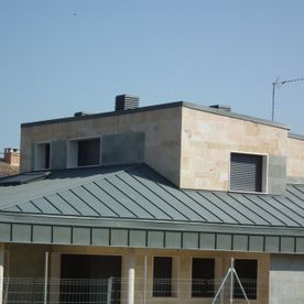 Casa moderna con techo de metal gris oscuro, paredes color canela y múltiples ventanas oscuras.