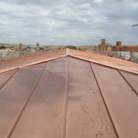 Techo de cobre con una ciudad al fondo bajo un cielo nublado.