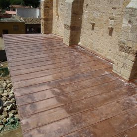 Techo de paneles de cobre junto a un muro de piedra. Paneles rectangulares marrones. Exterior soleado.