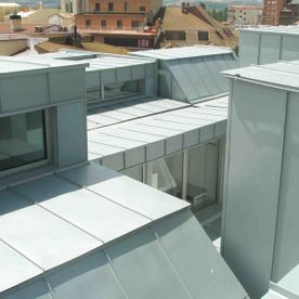 Techos de metal gris en un edificio moderno, vistos desde arriba, con edificios circundantes visibles en el fondo.