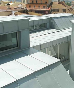 Exterior de edificio moderno con techo de metal gris en ángulo y paredes con ventanas.