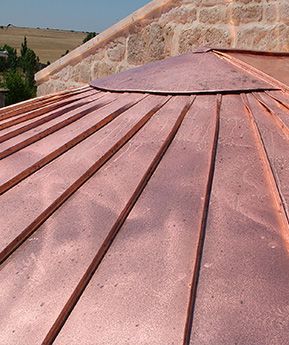 Techo de cobre con juntas elevadas y pared de piedra al fondo.