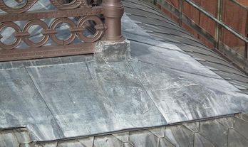 Primer plano de un techo de metal desgastado con barandilla decorativa y base de chimenea.