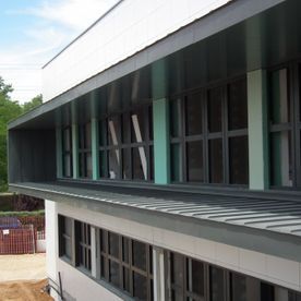 Exterior de edificio moderno con ventanas grandes, molduras oscuras y detalles en color verde azulado.