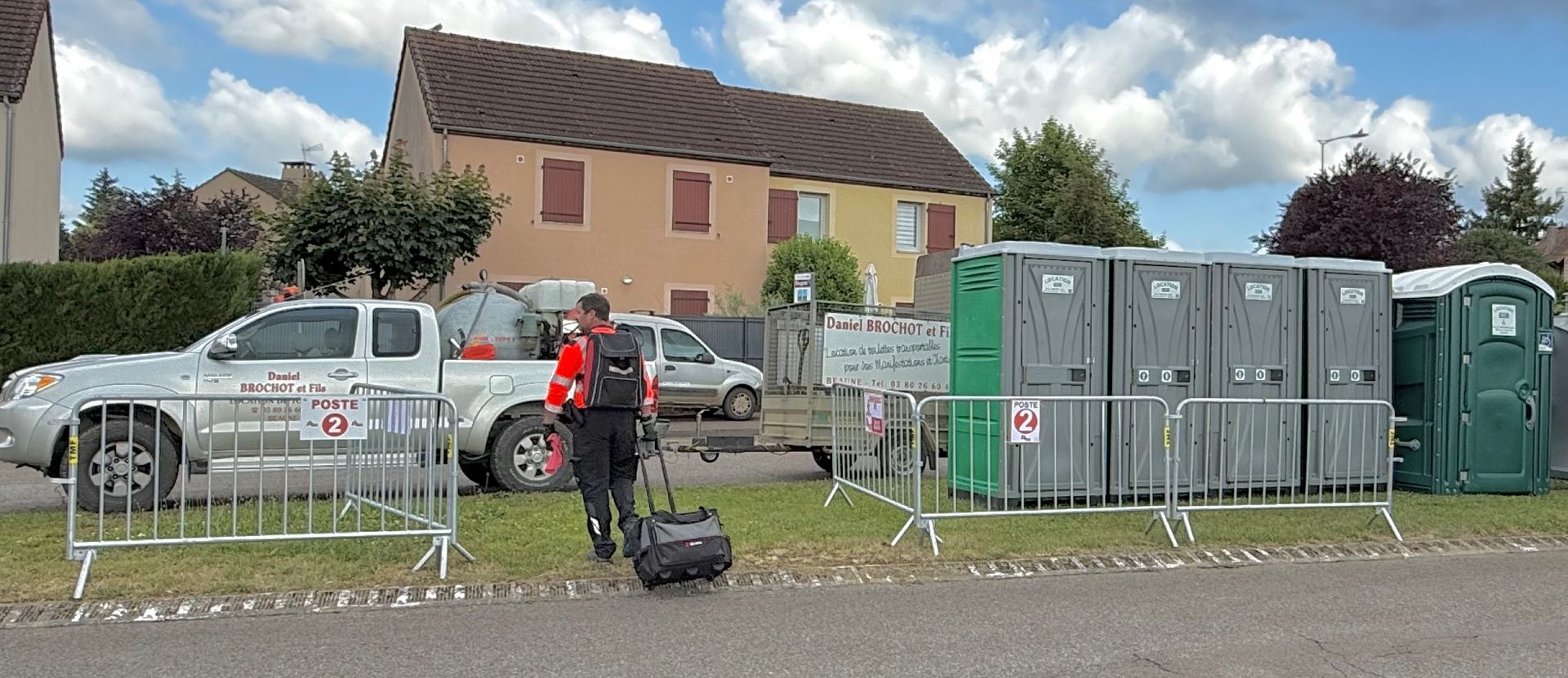 Homme avec une valise et gilet de sécurité à côté de WC mobiles