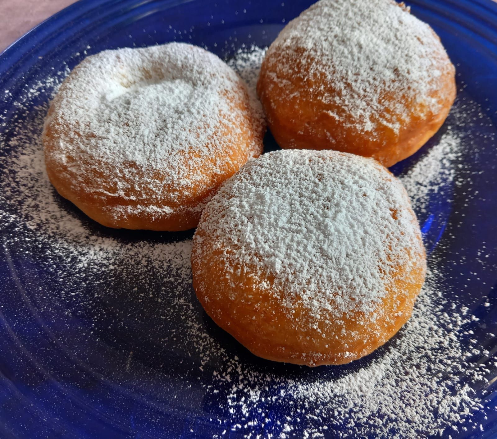 Tres donas cubiertas de azúcar en polvo en un plato azul