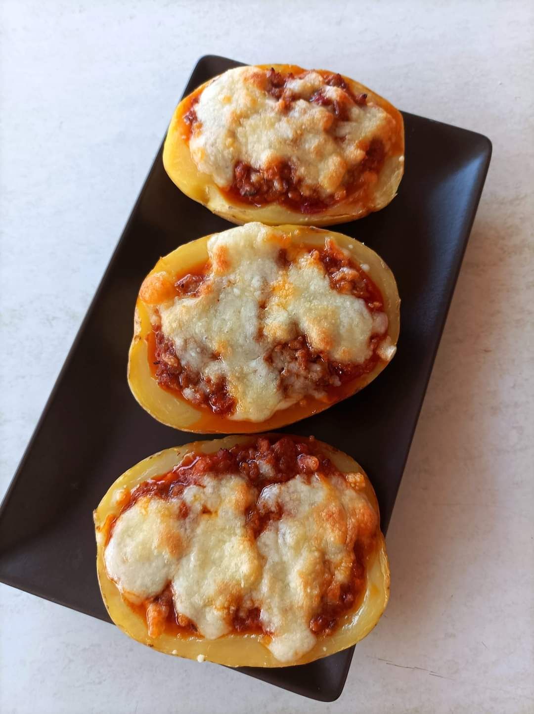 Tres pizzas de patata en un plato negro sobre una mesa