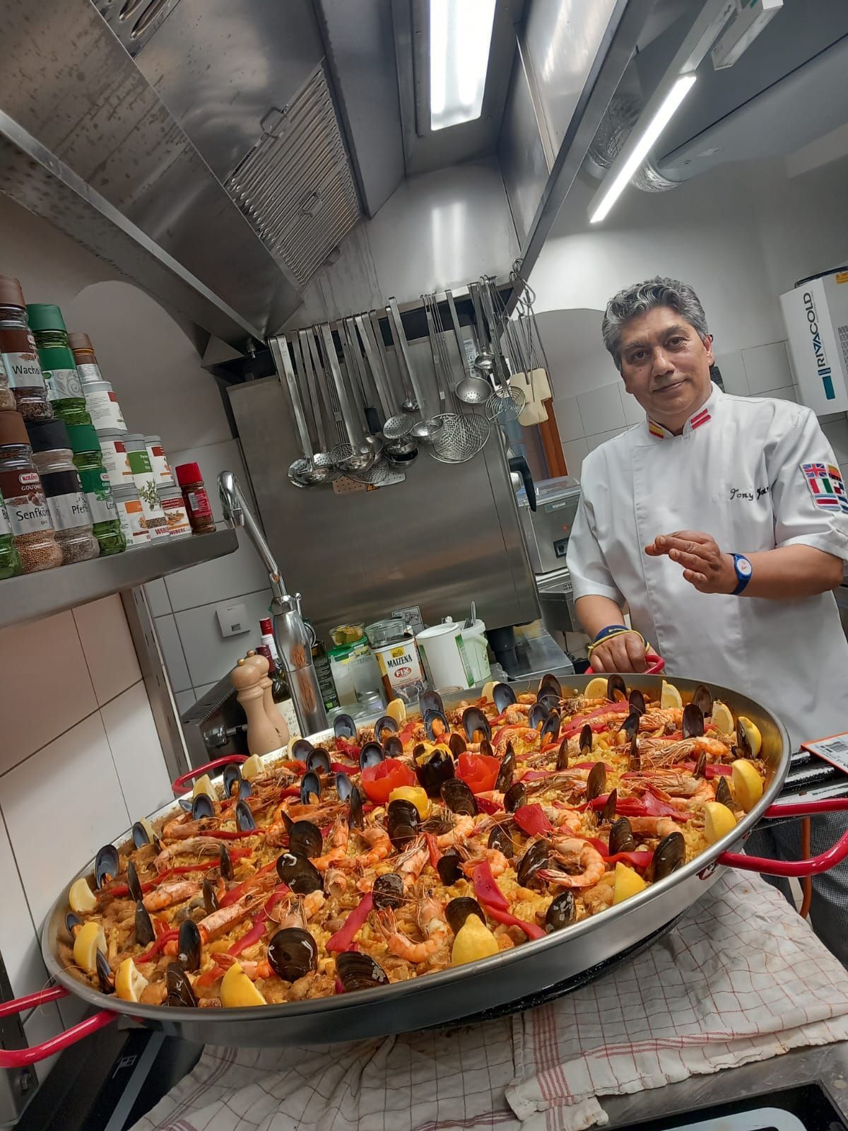 Un chef está de pie junto a una gran sartén de comida en una cocina.