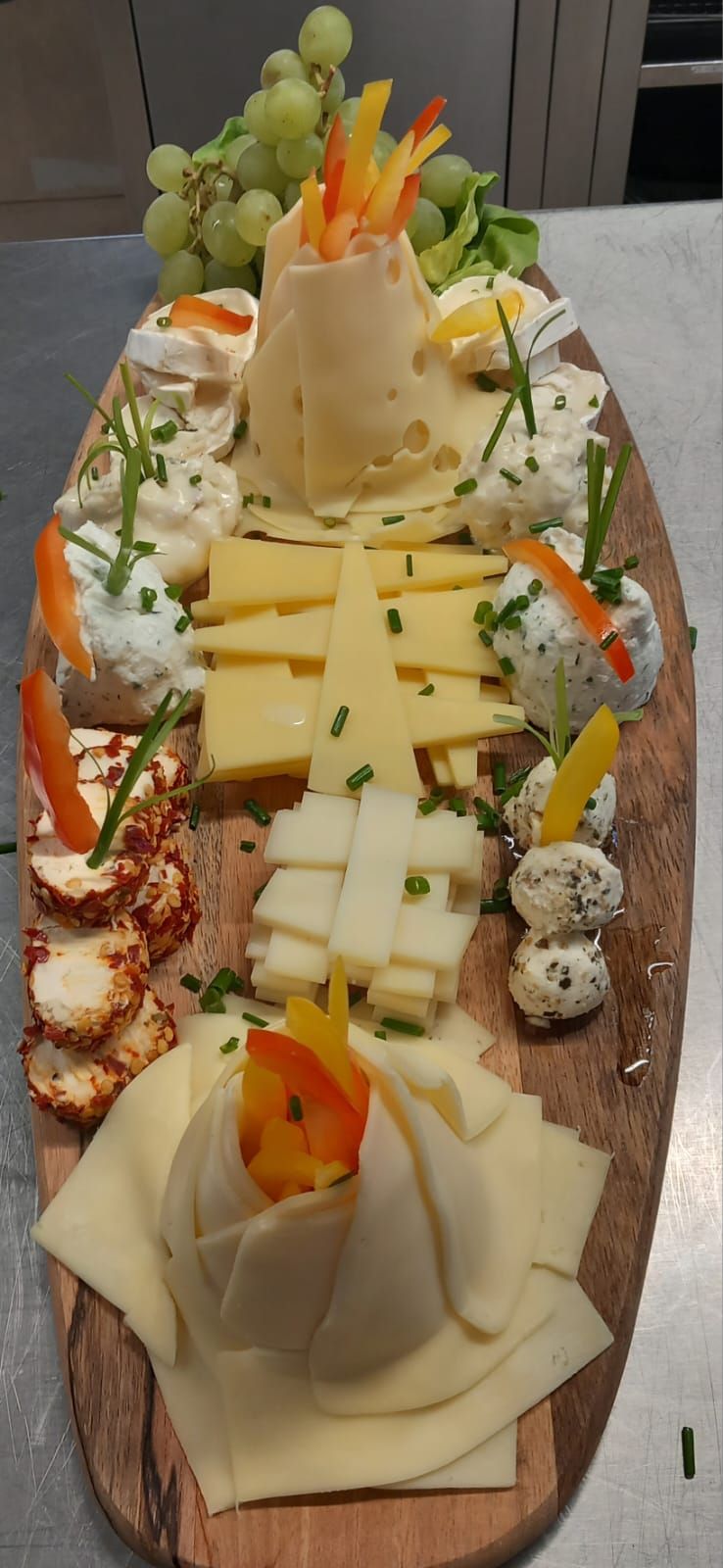 Una tabla de cortar de madera llena de una variedad de quesos y verduras.