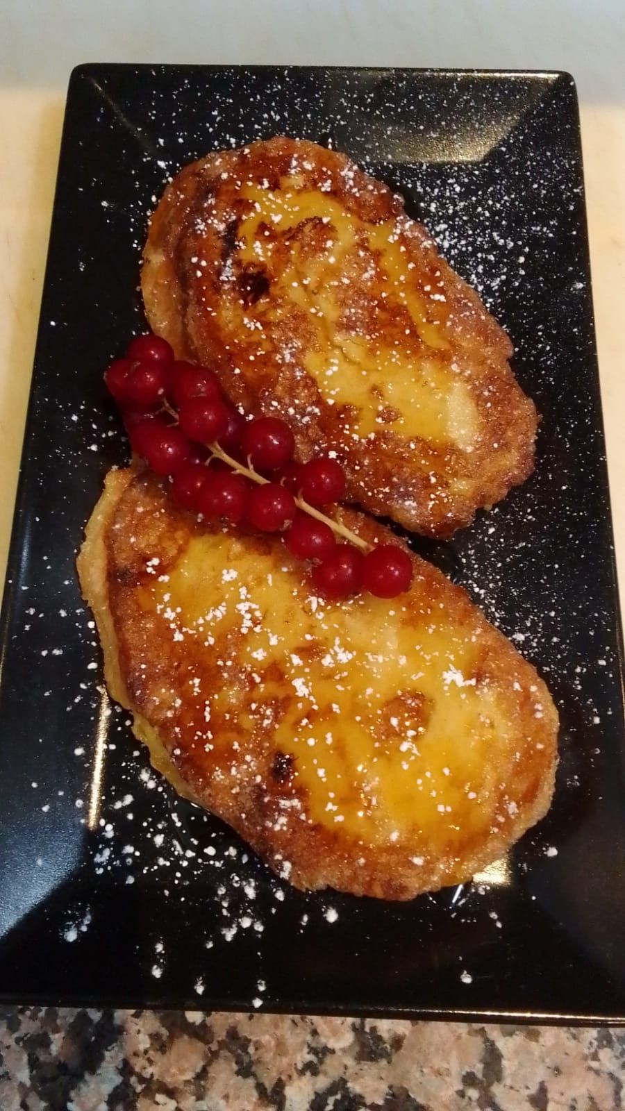 Tostada francesa con azúcar glas y grosellas rojas en un plato negro
