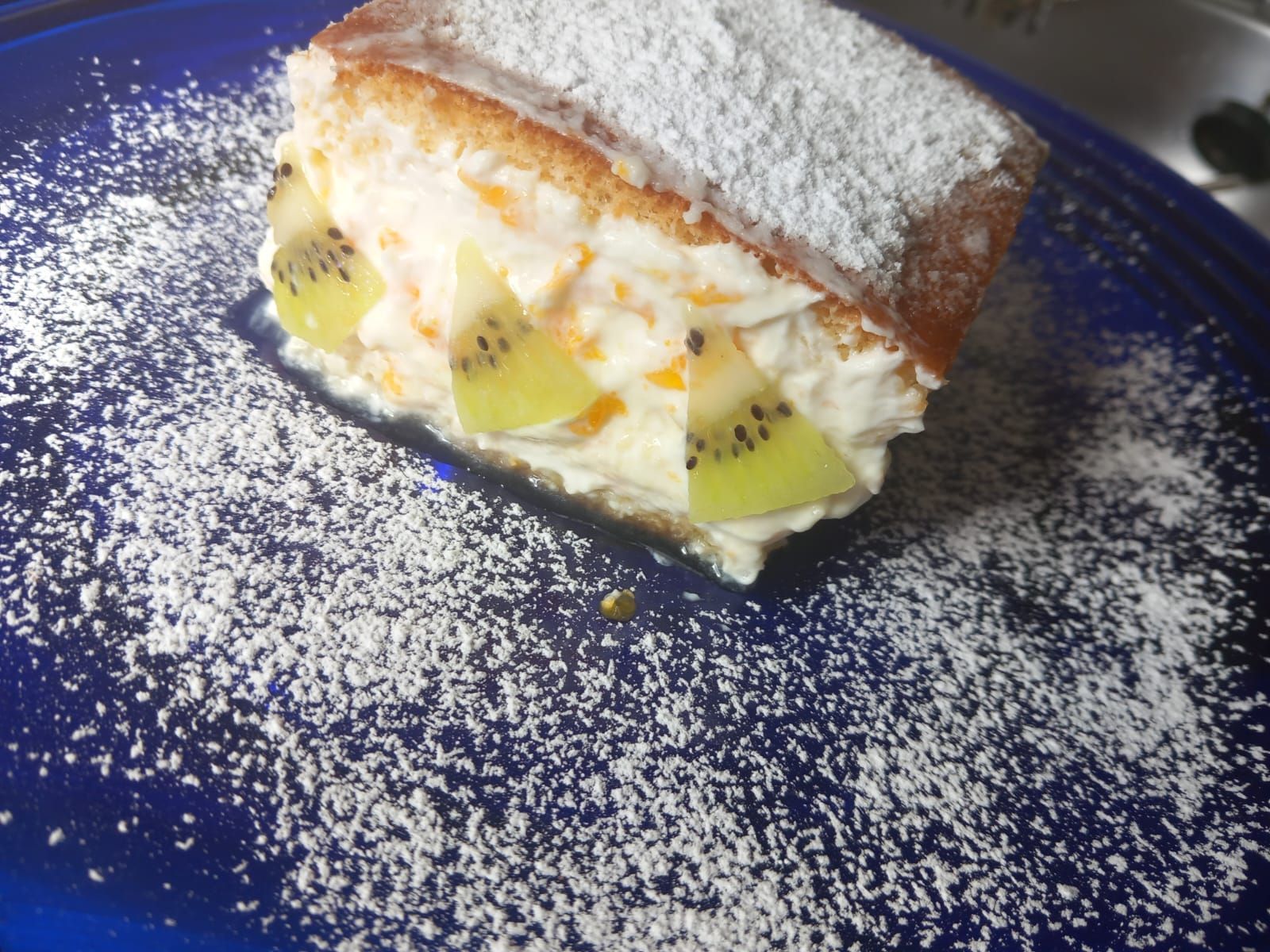 Un plato azul cubierto con un trozo de pastel y azúcar en polvo.
