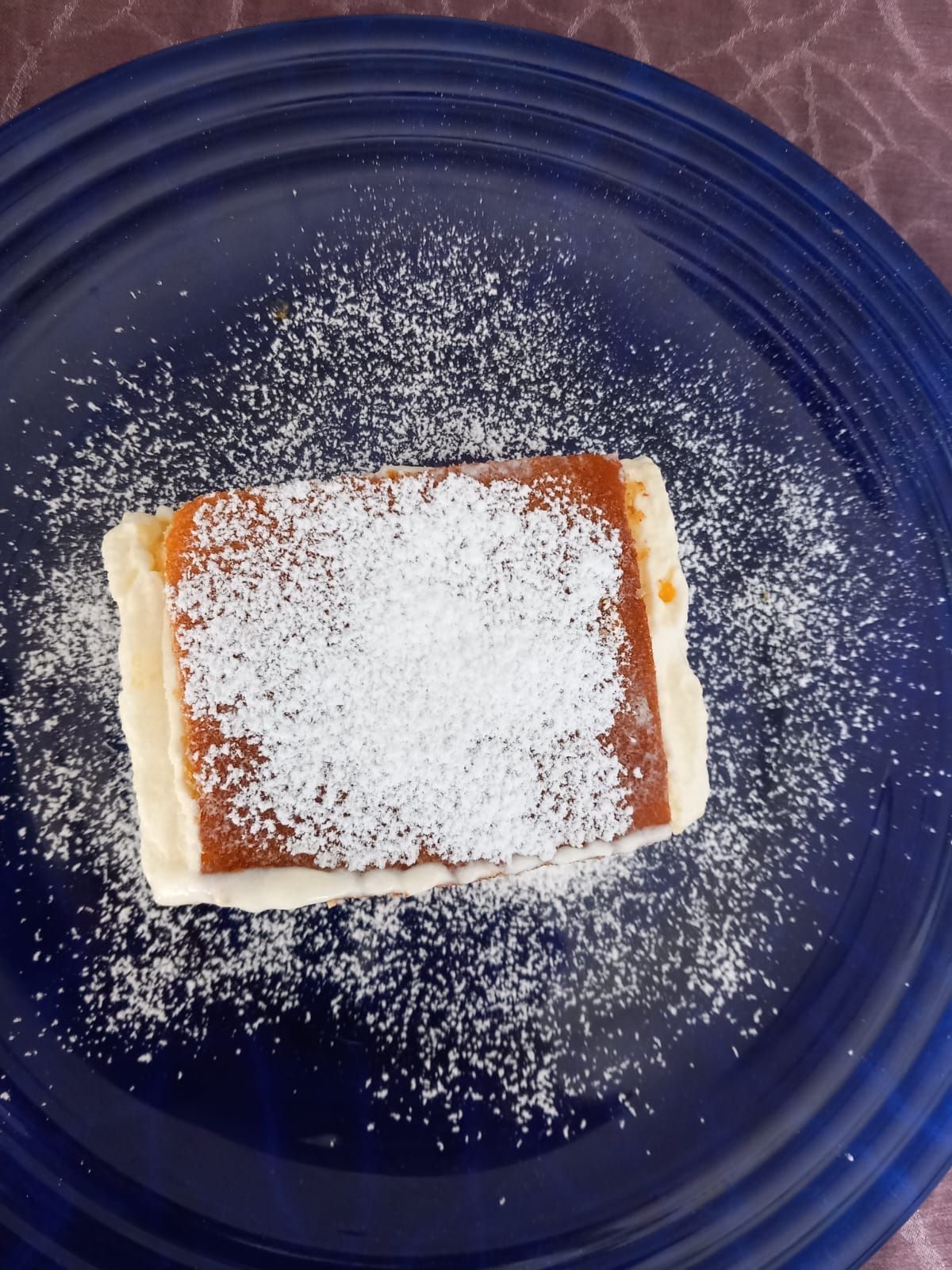 Un trozo de pastel en un plato azul con azúcar en polvo encima.